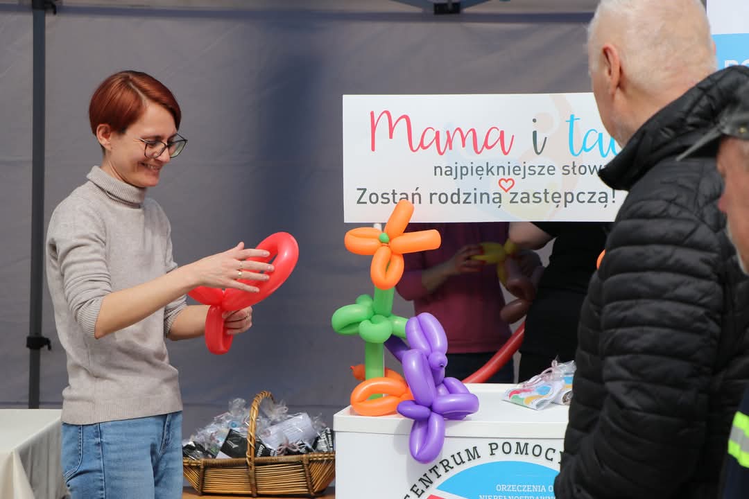 zdjęcia: na pierwszym planie pracownik pcpr z uśmiechem skręca baloniki